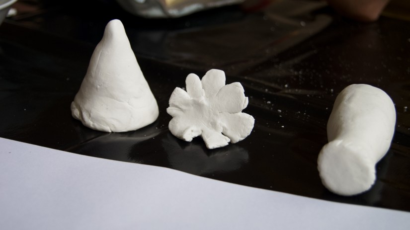 Drei der ersten fertigen Tonkunstwerke. Zu sehen sind ein Kegel, eine Blume und ein liegender Zylinder. 